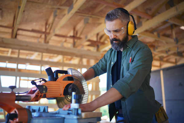 Construction worker working with the eletric saw inside wooden construction of house, diy eco-friendly homes concept.