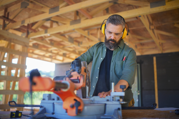 Construction worker working with eletric saw inside a wooden construction of house, diy eco-friendly homes concept.