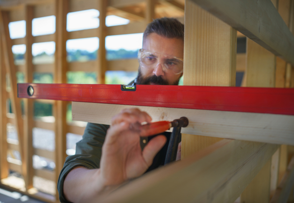 Carpenter checking a wooden planks with spirit level, diy eco-friendly homes concept.