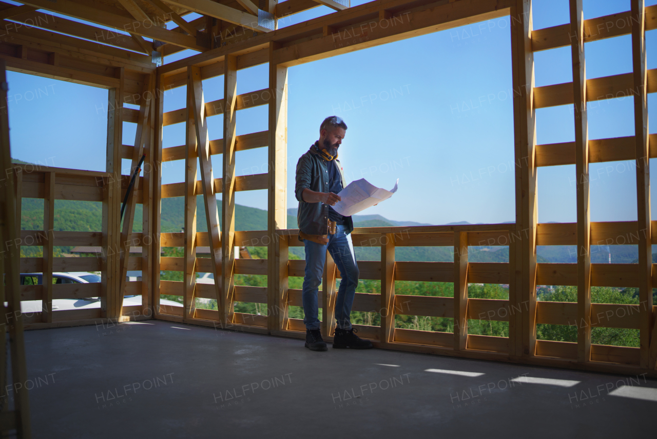 Handyman chcecking blueprints and working on a wooden construction site, diy eco-friendly homes concept.