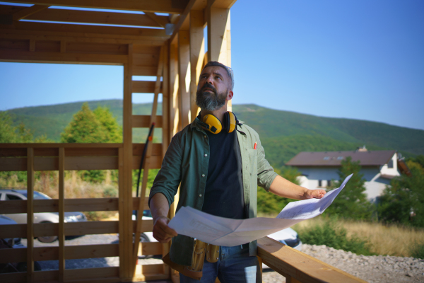 Handyman chcecking blueprints and working on a wooden construction site, diy eco-friendly homes concept.