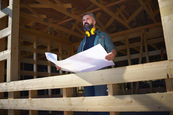 Handyman chcecking blueprints and working on a wooden construction site, diy eco-friendly homes concept.