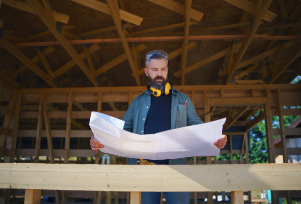 Handyman chcecking blueprints and working on a wooden construction site, diy eco-friendly homes concept.