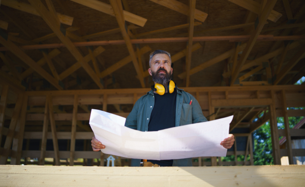 Handyman chcecking blueprints and working on a wooden construction site, diy eco-friendly homes concept.