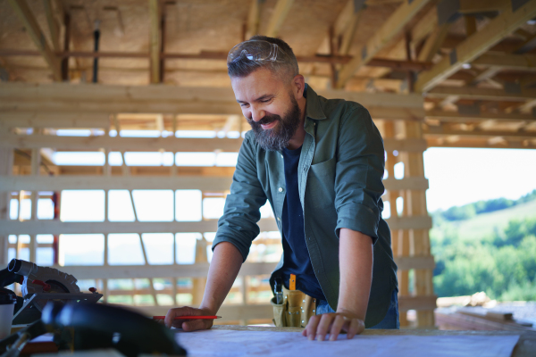 A portrait of construction worker smiling and checking blueprints, diy eco-friendly homes concept.