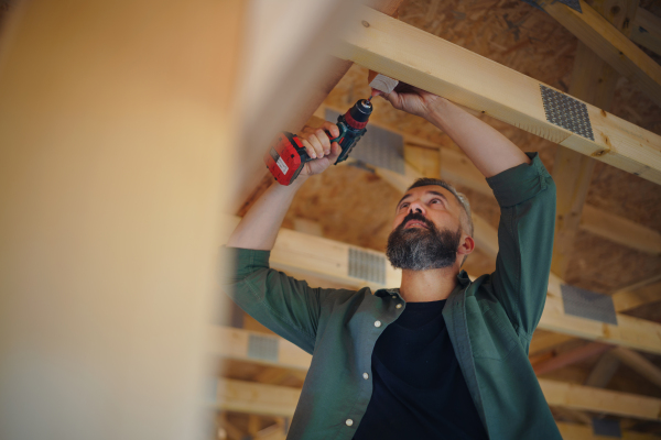 A construction worker working with screwdriver on wooden frame, diy eco-friendly homes concept.