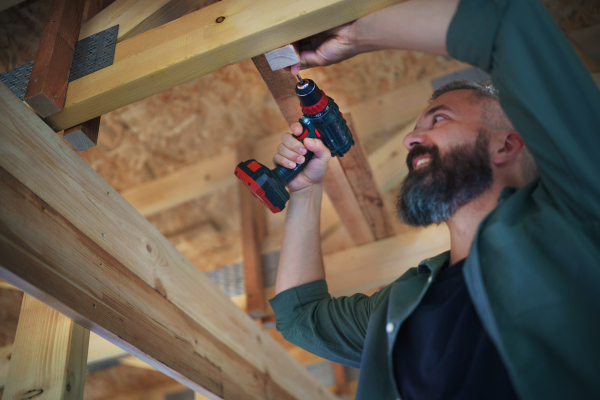 A construction worker working with screwdriver on wooden frame, diy eco-friendly homes concept.