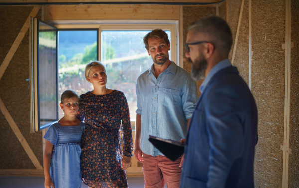 A sales agent showing plans of new house to young family on construction site.