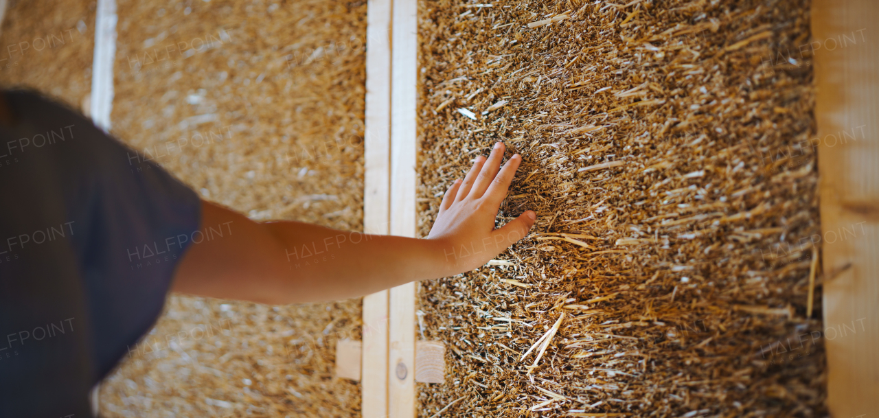 Close-up of a girl hand touching straw wooden eco house framing. Concept of sustainability and healthy living.