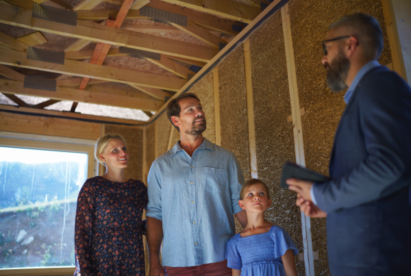 A sales Agent showing plans of new house to young family on construction site.