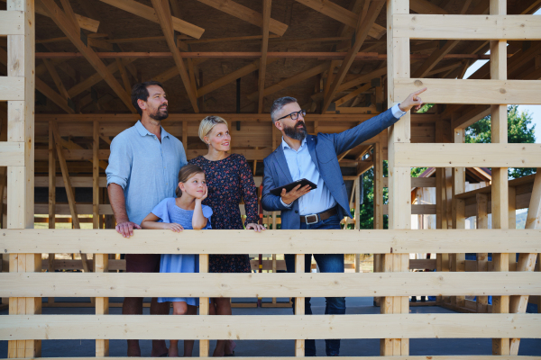 Sales agent showing plans of a new house to young family on construction site.