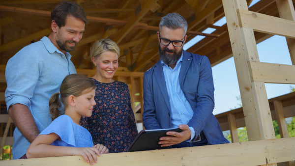 A sales Agent showing plans of new house to young family on construction site.