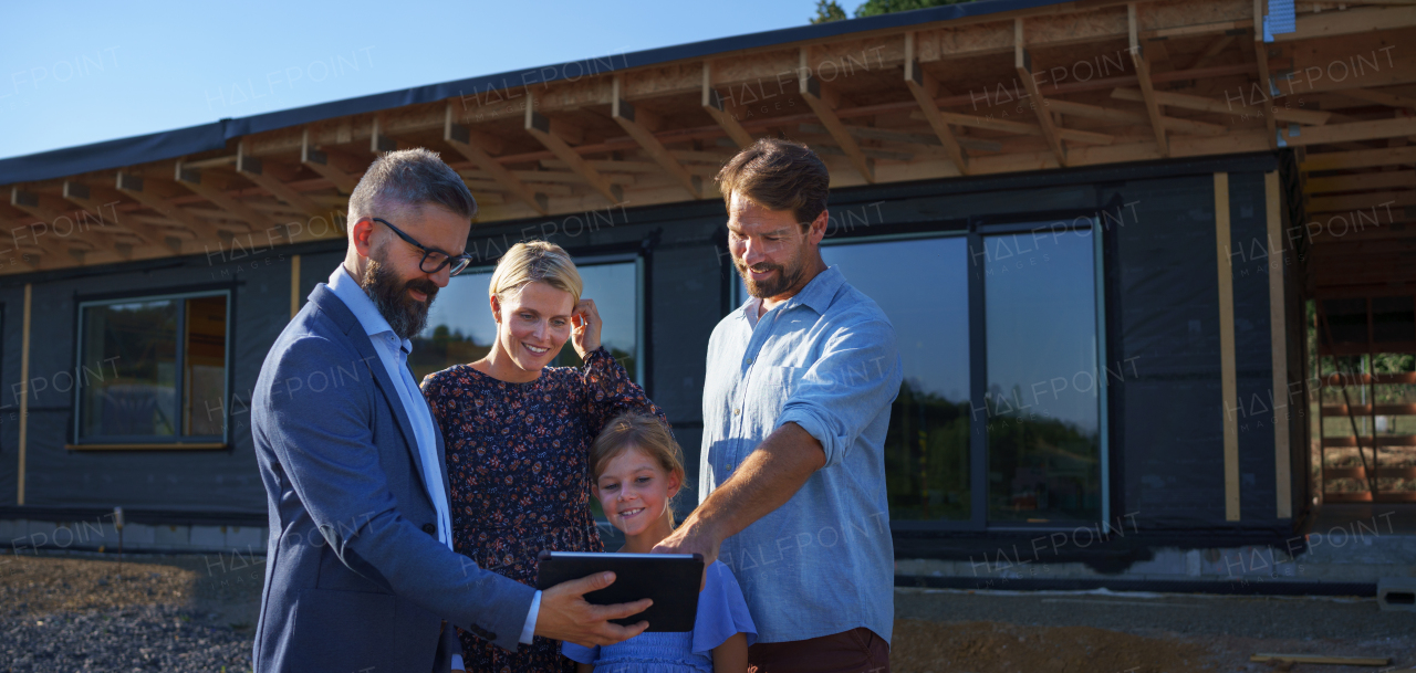 A sales Agent showing plans of new house to young family on construction site.