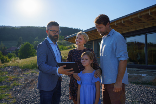 A sales Agent showing plans of new house to young family on construction site.