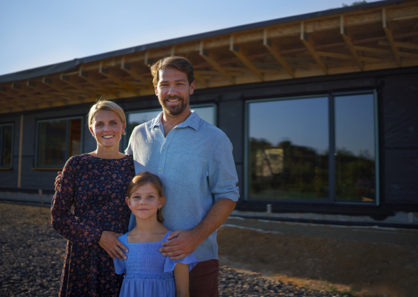 Young family standing in front of their ecologic wooden house, concept of sustainability and healthy living.