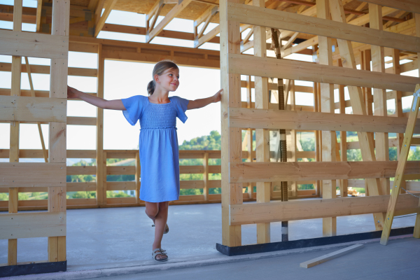 A little girl standing in wooden construction of their unfinished wooden eco house.