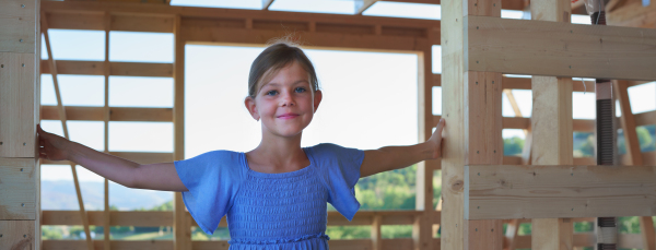 Portrait of little girl in wooden construction of their unfinished wooden eco house.