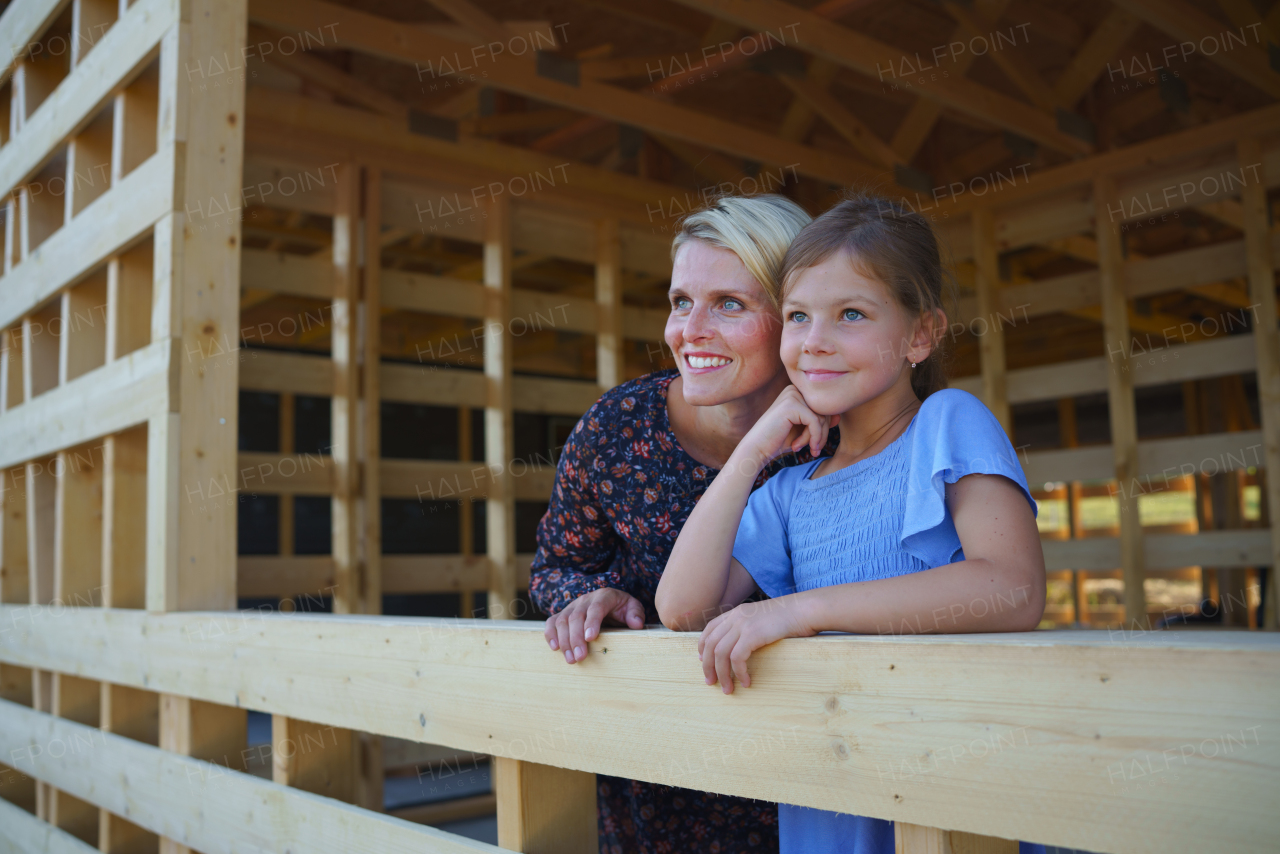 Mother and daughterr on site inside of new ecology wooden home construction framing.