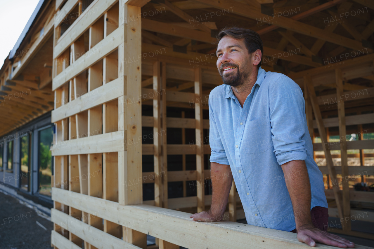 Man looking out of his unfinished house, construction of ecological renewable low energy sustainable wooden eco house .