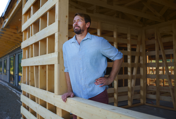 Man looking out of the unfinished house, construction of ecological renewable low energy sustainable wooden eco house .