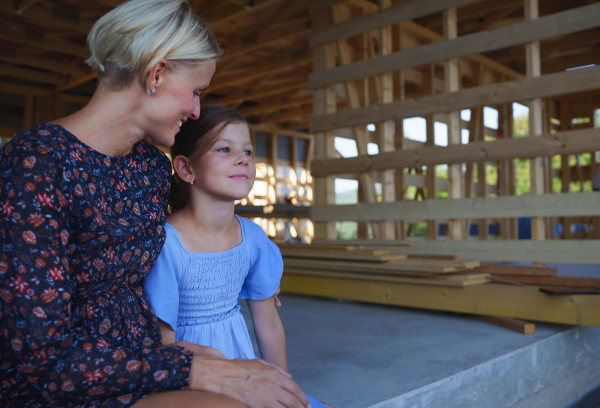 Mother and daughter on site inside of new ecology wooden home construction framing.