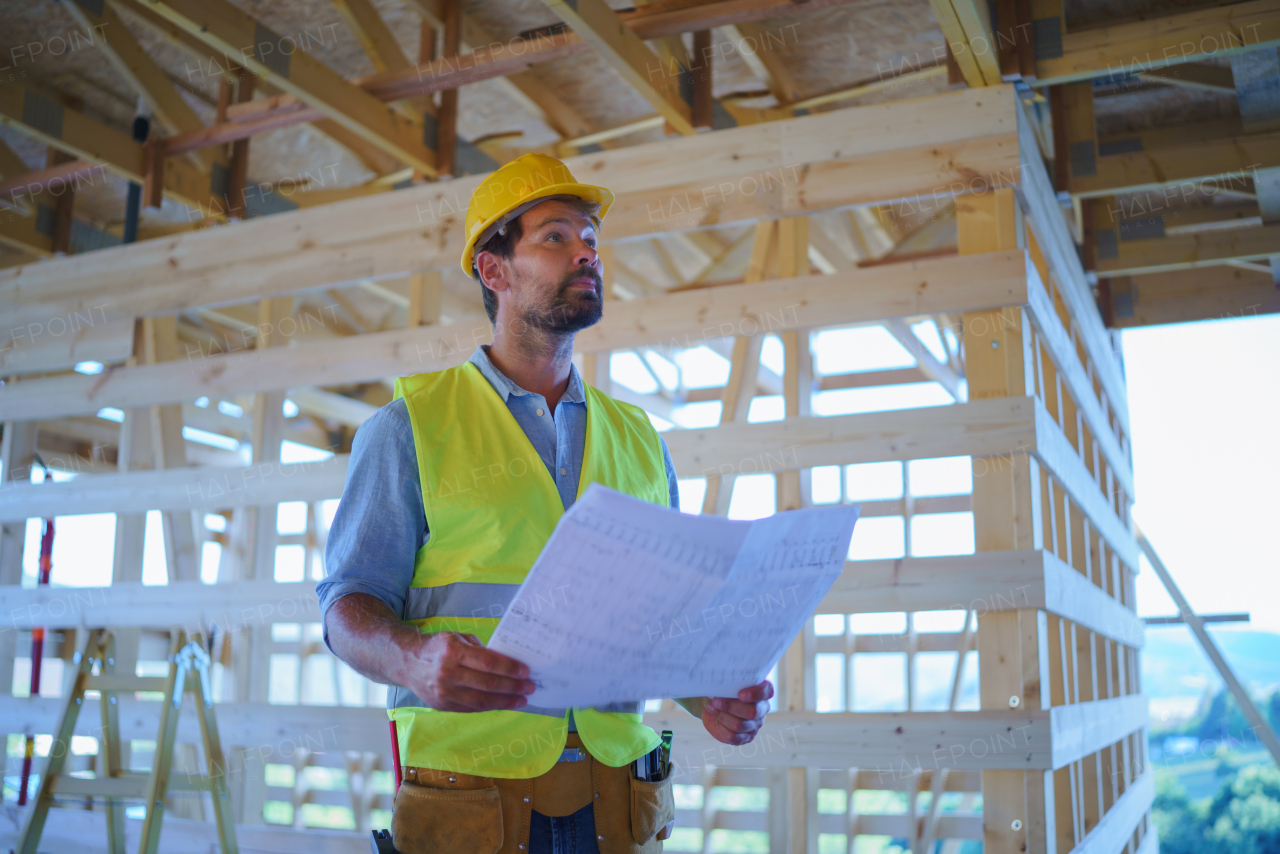 Construction engineer or architect with blueprints visiting and checking a building site of wood frame house