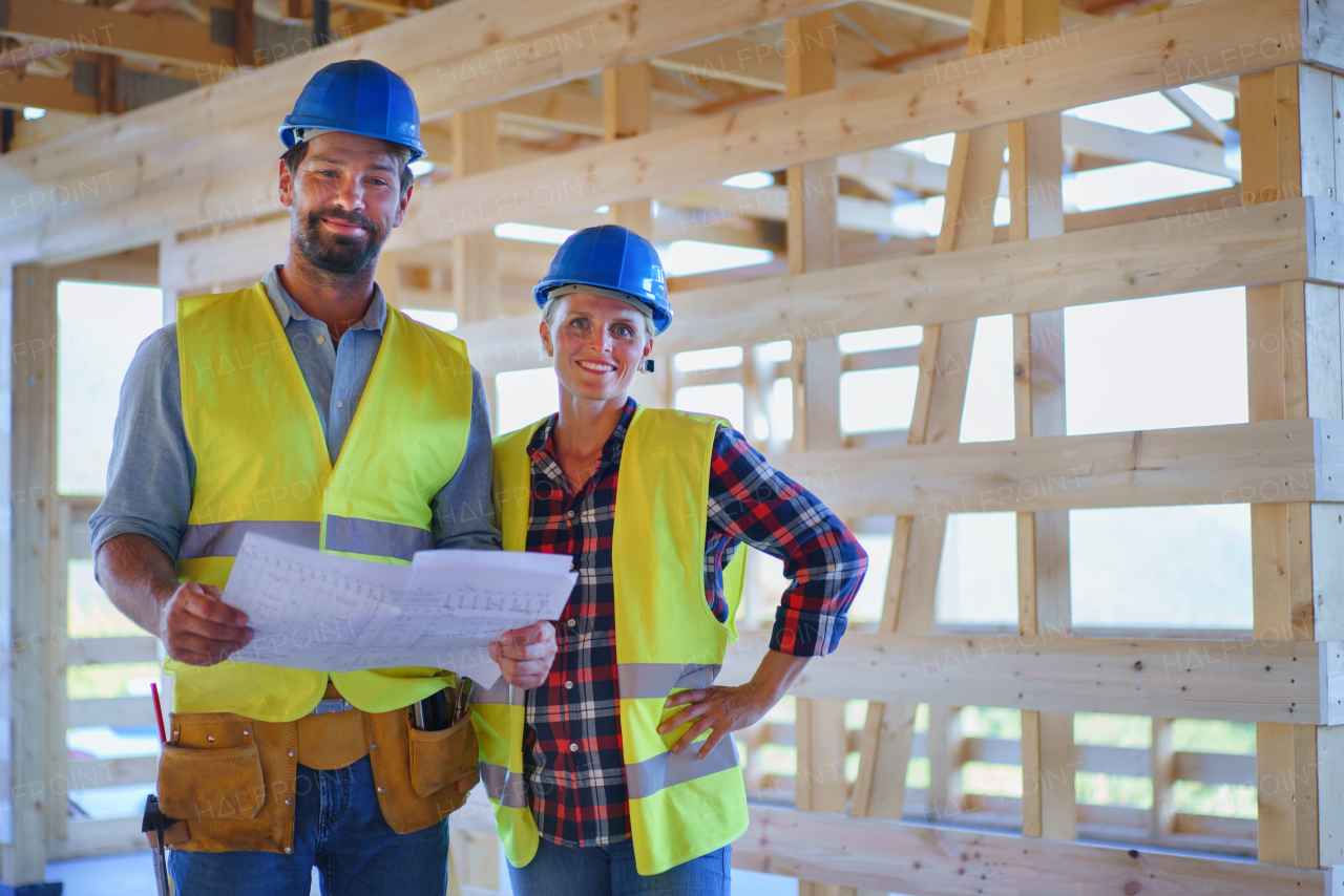 Construction engineers or architects with blueprints visiting a building site of wood frame house