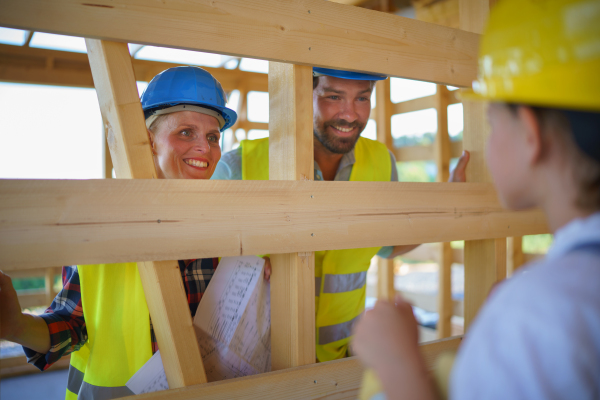 Cheerful family in protective clothes checking their unfinished eco wooden house, concept of sustainability and healthy living.