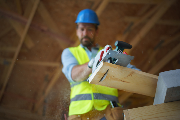 A low angle view of handyman working with circular saw on wooden construction site, diy eco-friendly homes concept.