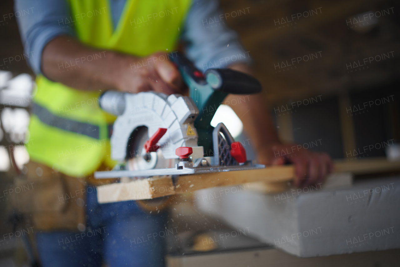 Close-up of construction worker working with eletric saw inside a wooden construction of house, diy eco-friendly homes concept.