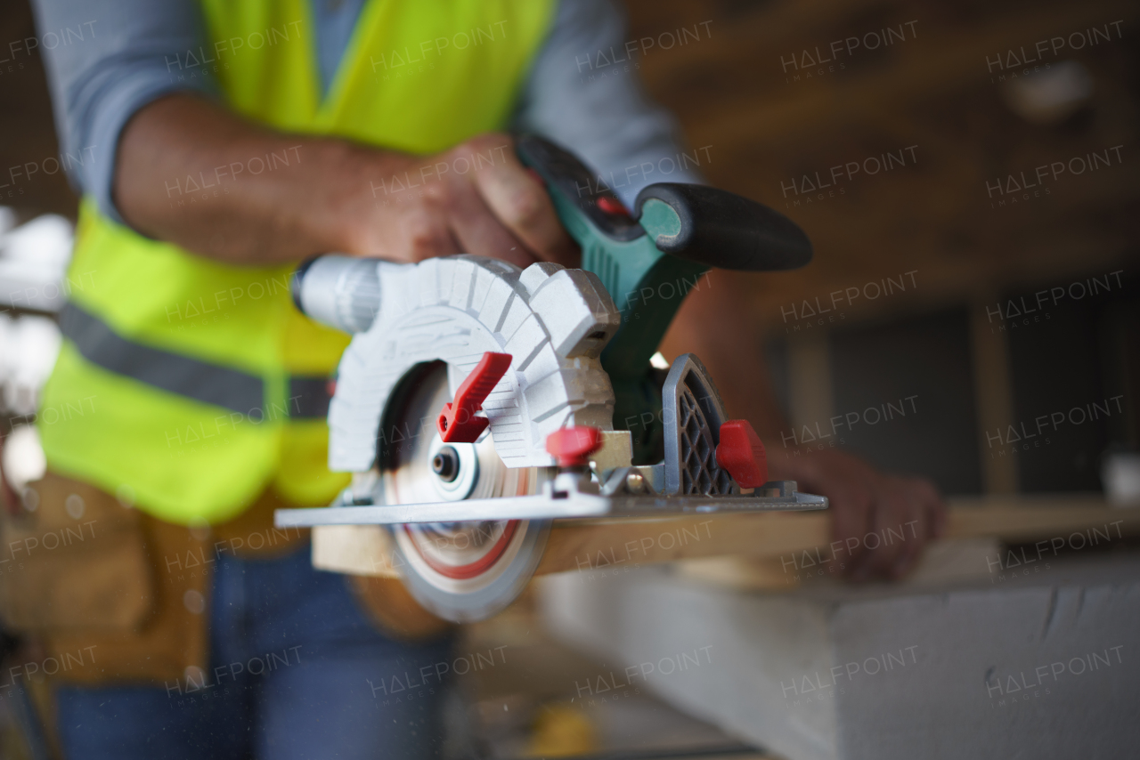 Close-up of construction worker working with the eletric saw inside wooden construction of house, diy eco-friendly homes concept.