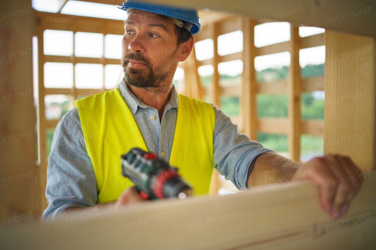 A construction worker working with electric screwdriver on wooden frame, diy eco-friendly homes concept.