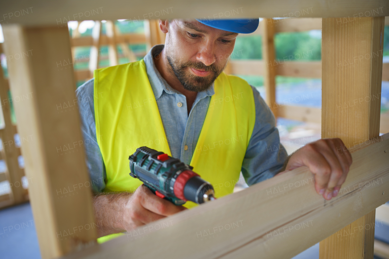 A construction worker working with screwdriver on wooden frame, diy eco-friendly homes concept.