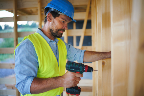 A construction worker working with screwdriver on wooden frame, diy eco-friendly homes concept.