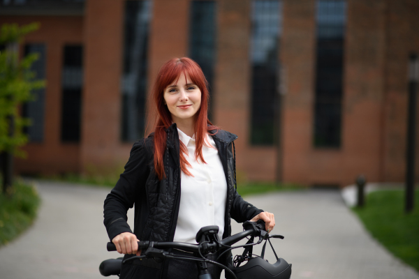 A portrait of businesswoman commuter on the way to work with bike looking at camera, sustainable lifestyle concept.