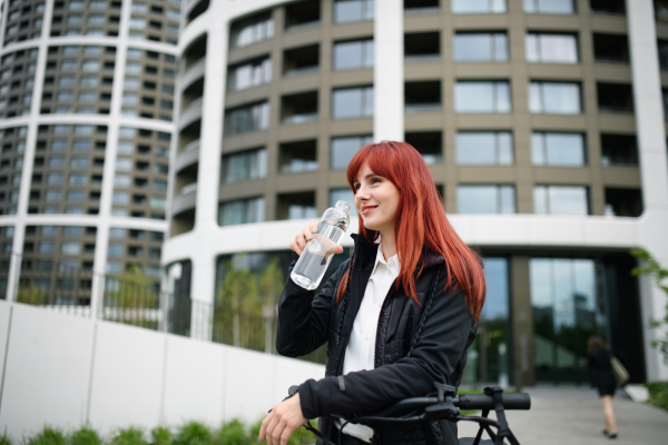 A portrait of businesswoman commuter on the way to work with bike, drinking water, sustainable lifestyle concept.