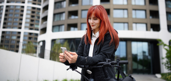 A portrait of businesswoman commuter on the way to work with bike, using smartphone, sustainable lifestyle concept.