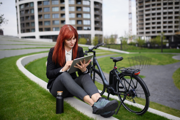 A businesswoman with bike sitting on stairs and using tablet. Commuting and alternative transport concept