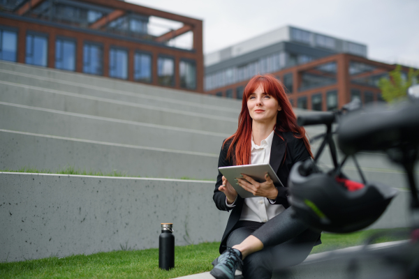 A businesswoman with bike sitting on stairs and using tablet. Commuting and alternative transport concept