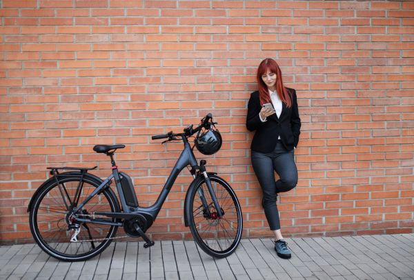 A portrait of businesswoman commuter on the way to work with bike, using smartphone, sustainable lifestyle concept.