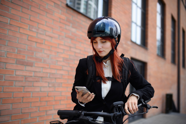 A portrait of businesswoman commuter on the way to work with bike, using smartphone, sustainable lifestyle concept.