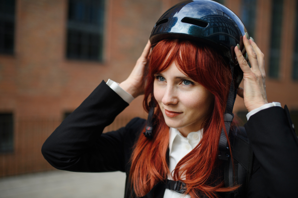 A portrait of businesswoman commuter on the way to work putting on cycling helmet, sustainable lifestyle concept.