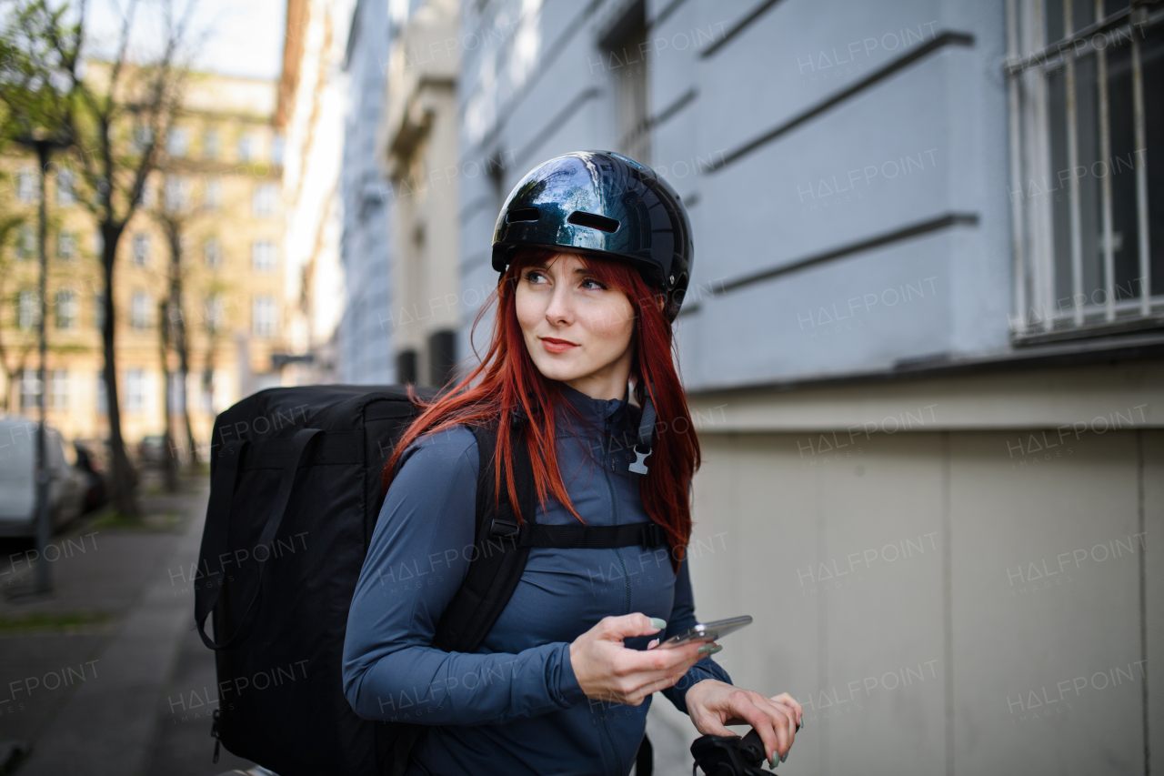 A female courier on bicycle with thermal backpack on way to deliver food to customers.