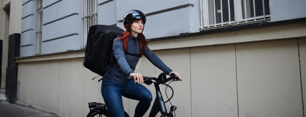 A female courier on bicycle with thermal backpack on way to deliver food to customers.