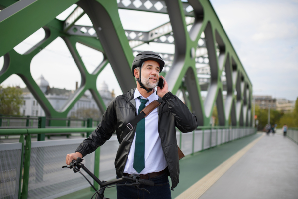 A portrait of businessman commuter on the way to work, pushing bike and calling on mobile phone, sustainable lifestyle concept.