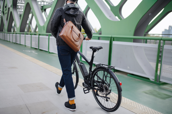 A rear view of businessman commuter on the way to work, pushing bike, sustainable lifestyle concept.