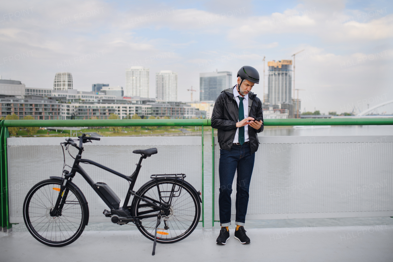 A businessman commuter on the way to work, standing on bridge and texting on mobile phone, sustainable lifestyle concept.