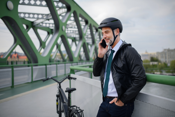 A businessman commuter on the way to work, on bridge, calling on mobile phone, sustainable lifestyle concept.