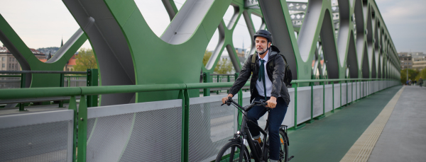 A businessman commuter on the way to work, riding bike over bridge, sustainable lifestyle concept. Wide shot.