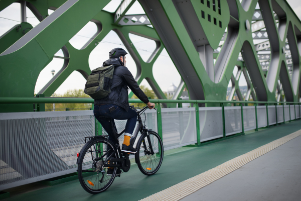 Rear view of a businessman commuter on the way to work, riding bike over bridge, sustainable lifestyle concept.